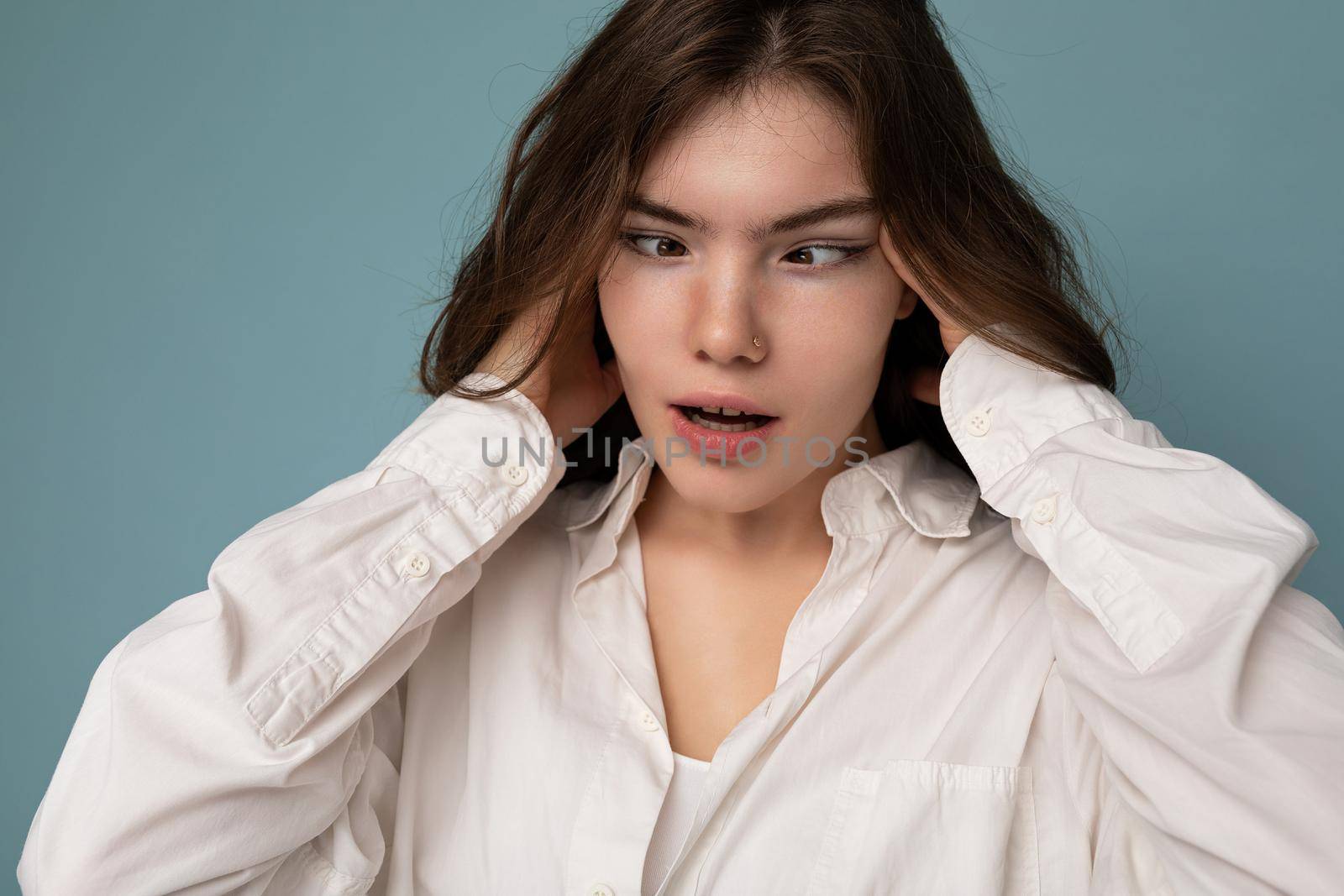 Attractive funny amusing joyful cute nice adorable tender young curly brunette woman wearing white shirt isolated on blue background with copy space.