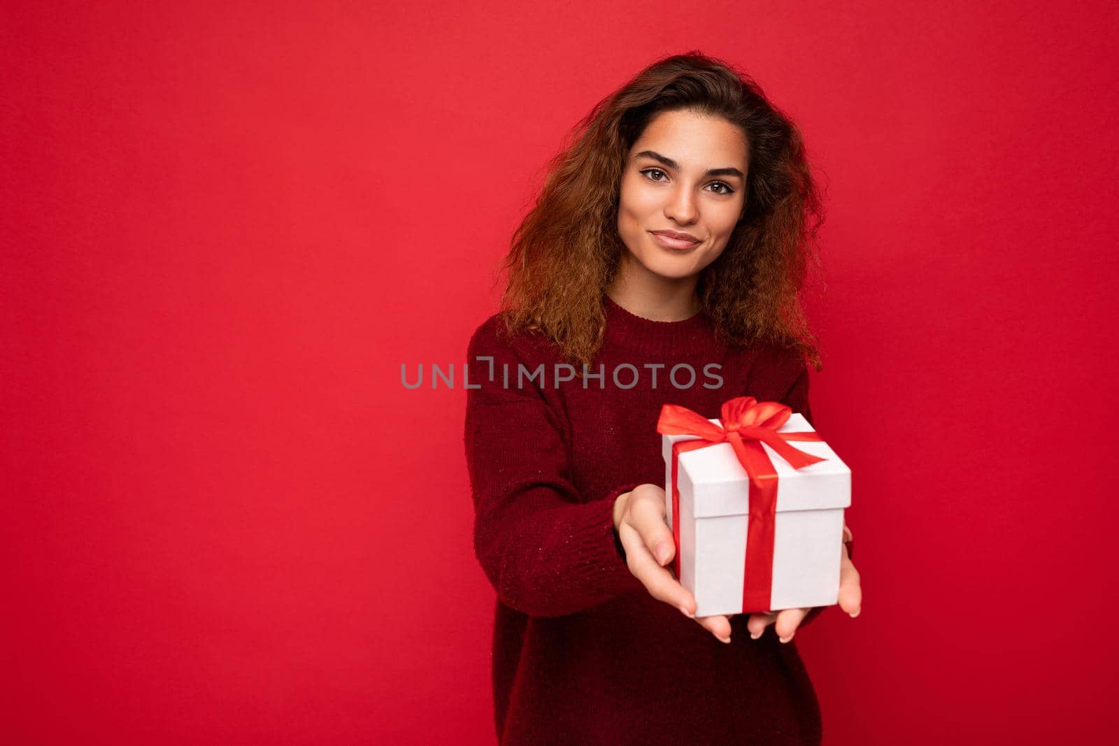 Shot of attractive positive smiling young brunette woman isolated over colourful background wall wearing everyday trendy outfit holding gift box and looking at camera. Copy space, mockup