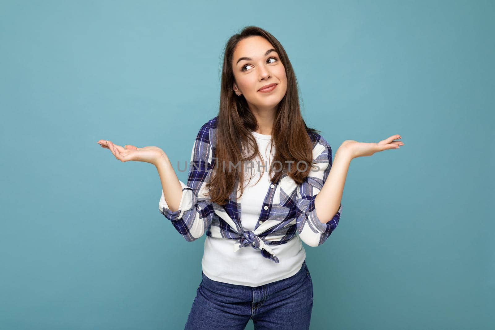 Photo of young positive happy smiling beautiful woman with sincere emotions wearing stylish clothes isolated over background with copy space and having doubts.