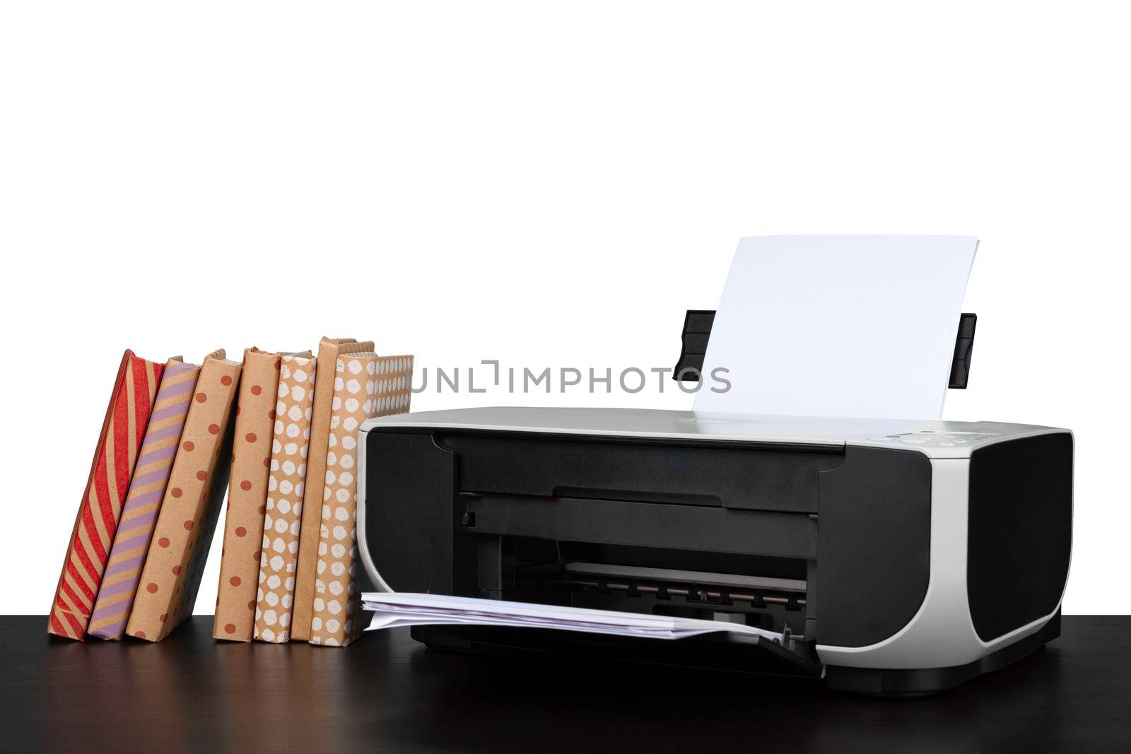 Printer and stack of books on black table against white background, close up