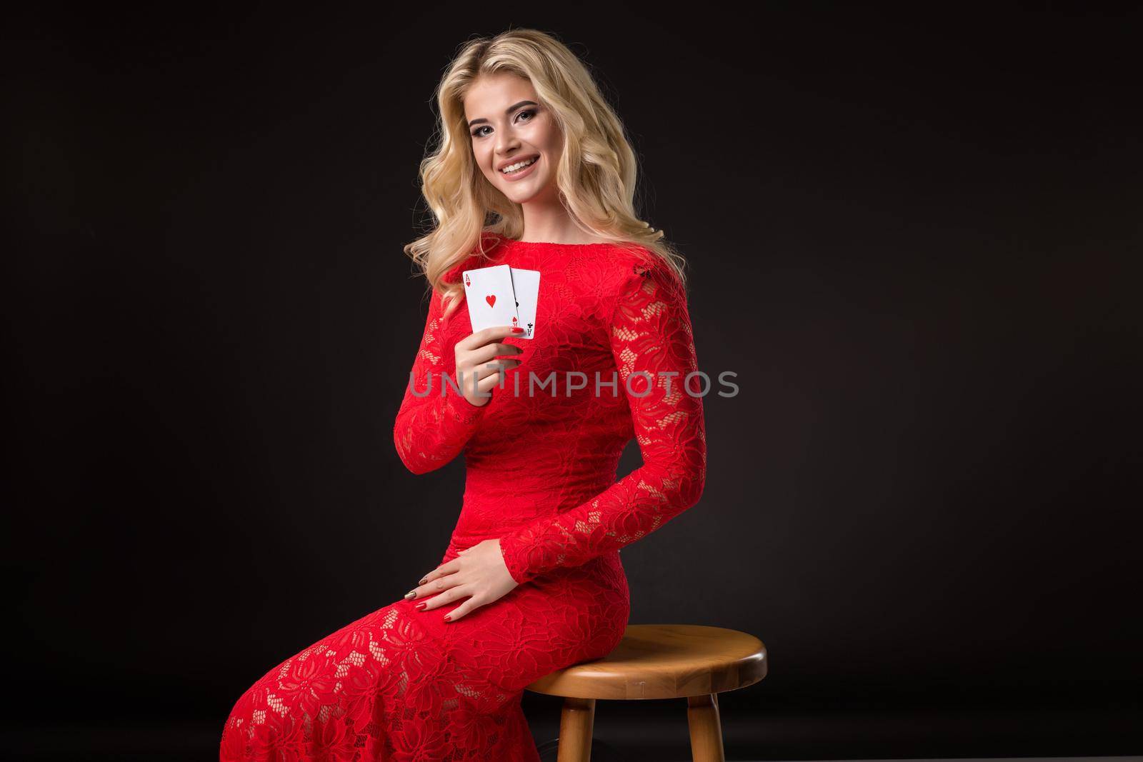 Young woman in red dress in casino with cards over black background. Poker