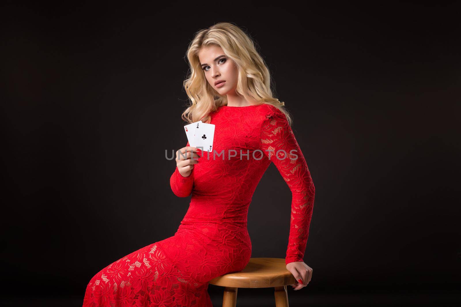 Young woman in red dress in casino with cards over black background. Poker