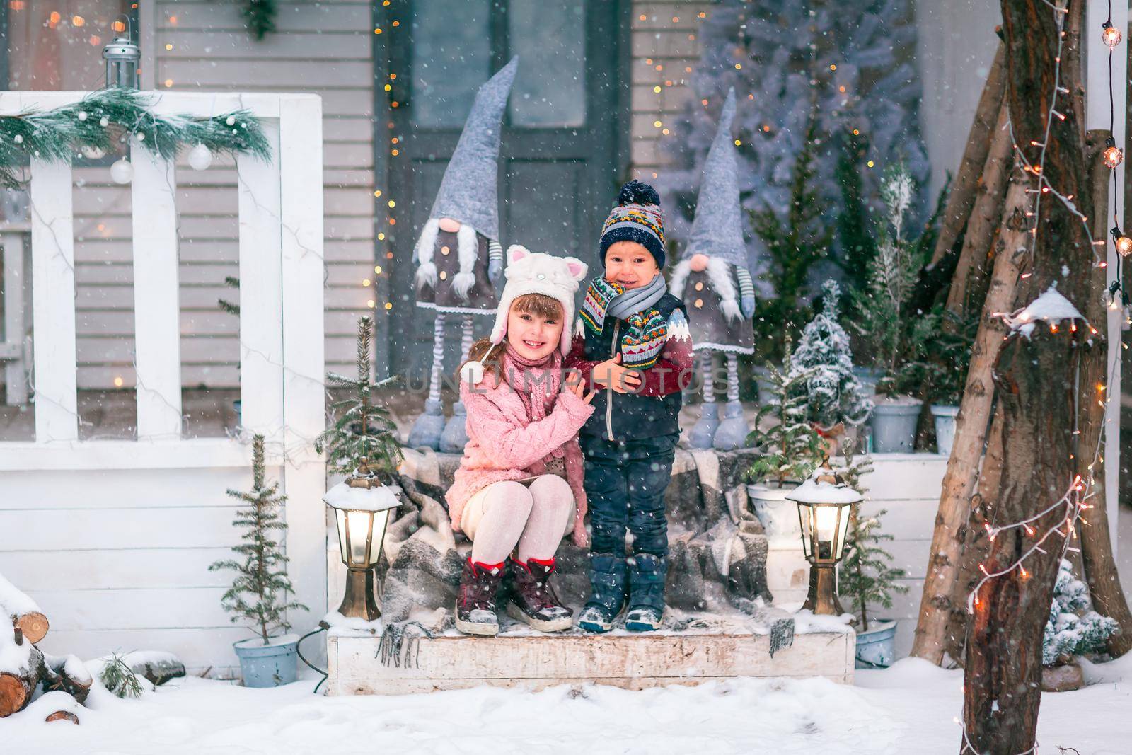 Happy little kids sitting on the porch of the Christmas decorated house outdoor by Len44ik