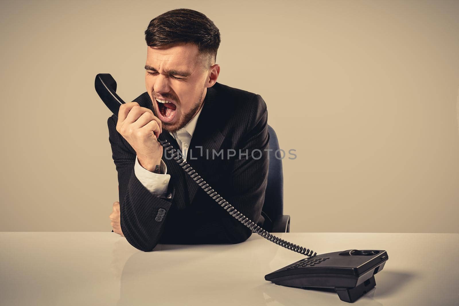 A young man in a black suit dials the phone number while sitting in the office. Manager talking on the phone. Man emotionally shouts