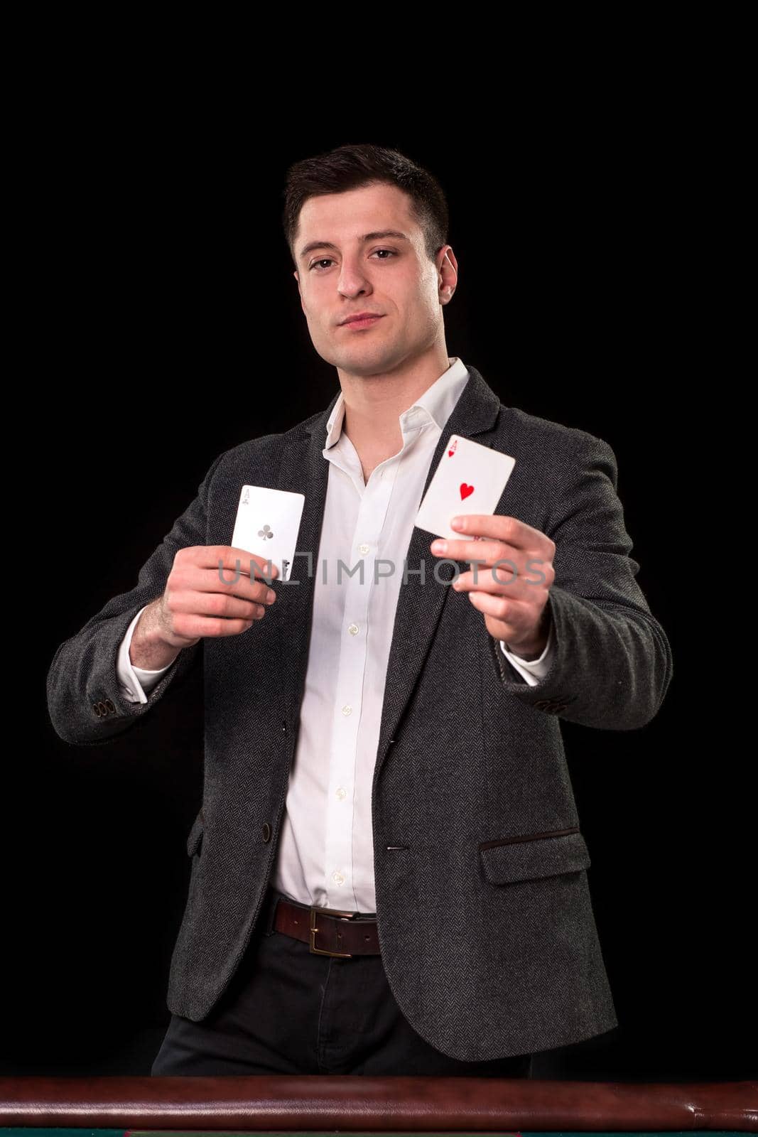 Young caucasian man in a dark suit and a white shirt holding two aces in his hands on black background. Gambling concept. Casino