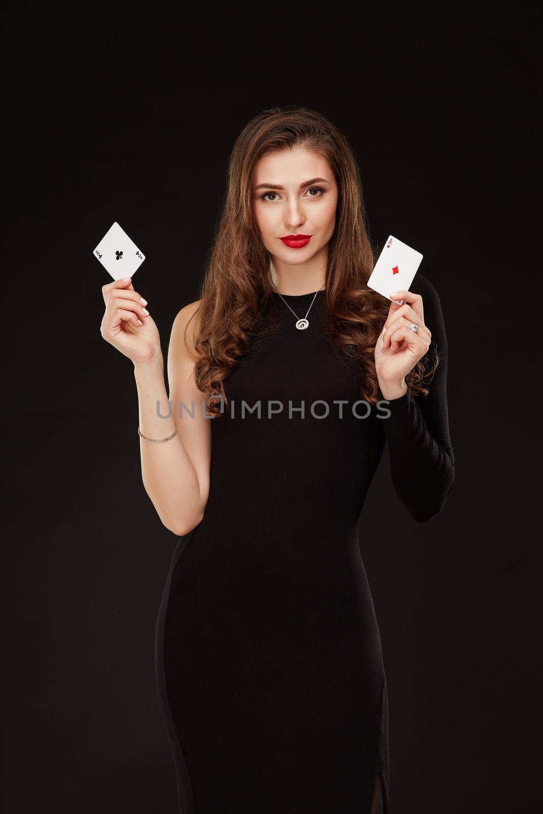 Attractive young woman in a sexy black dress holding the winning combination of poker cards. Two Aces. Studio shot on a black background. Casino