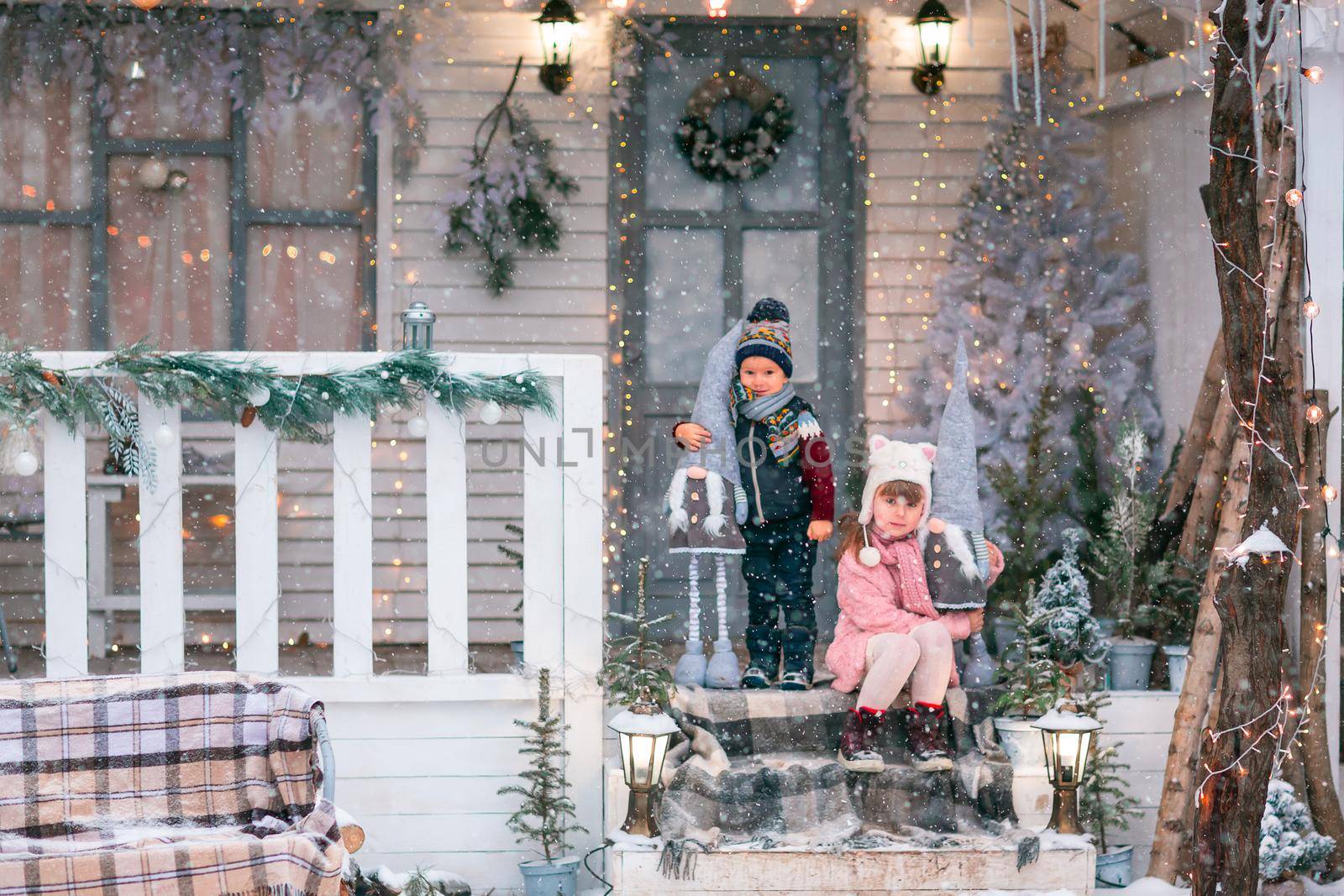 Happy little kids sitting on the porch of the Christmas decorated house outdoor by Len44ik