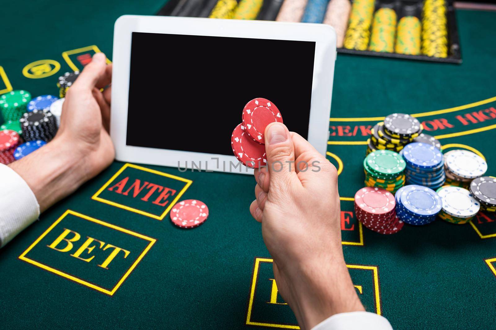 casino, online gambling, technology and people concept - close up of poker player with playing cards, tablet and chips at green casino table. first-person view. It makes chips bet