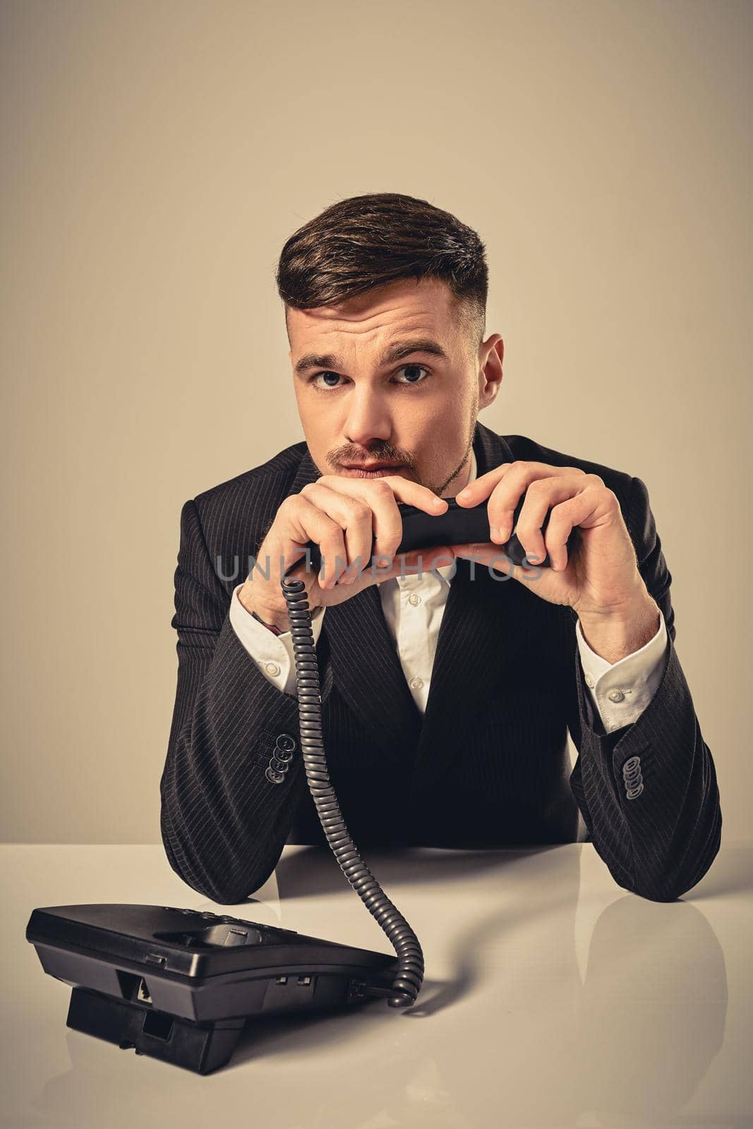 A young man in a black suit dials the phone number while sitting in the office. Manager looking at the camera and talking on the phone