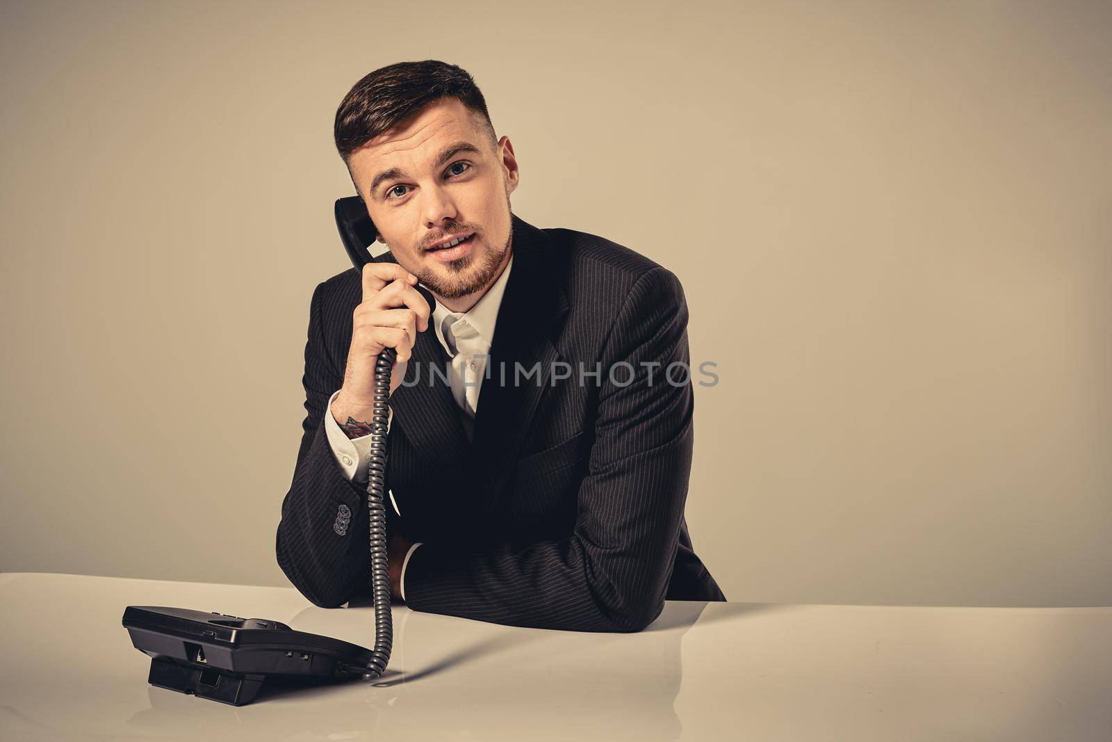 A young man in a black suit dials the phone number while sitting in the office. Manager looking at the camera and talking on the phone