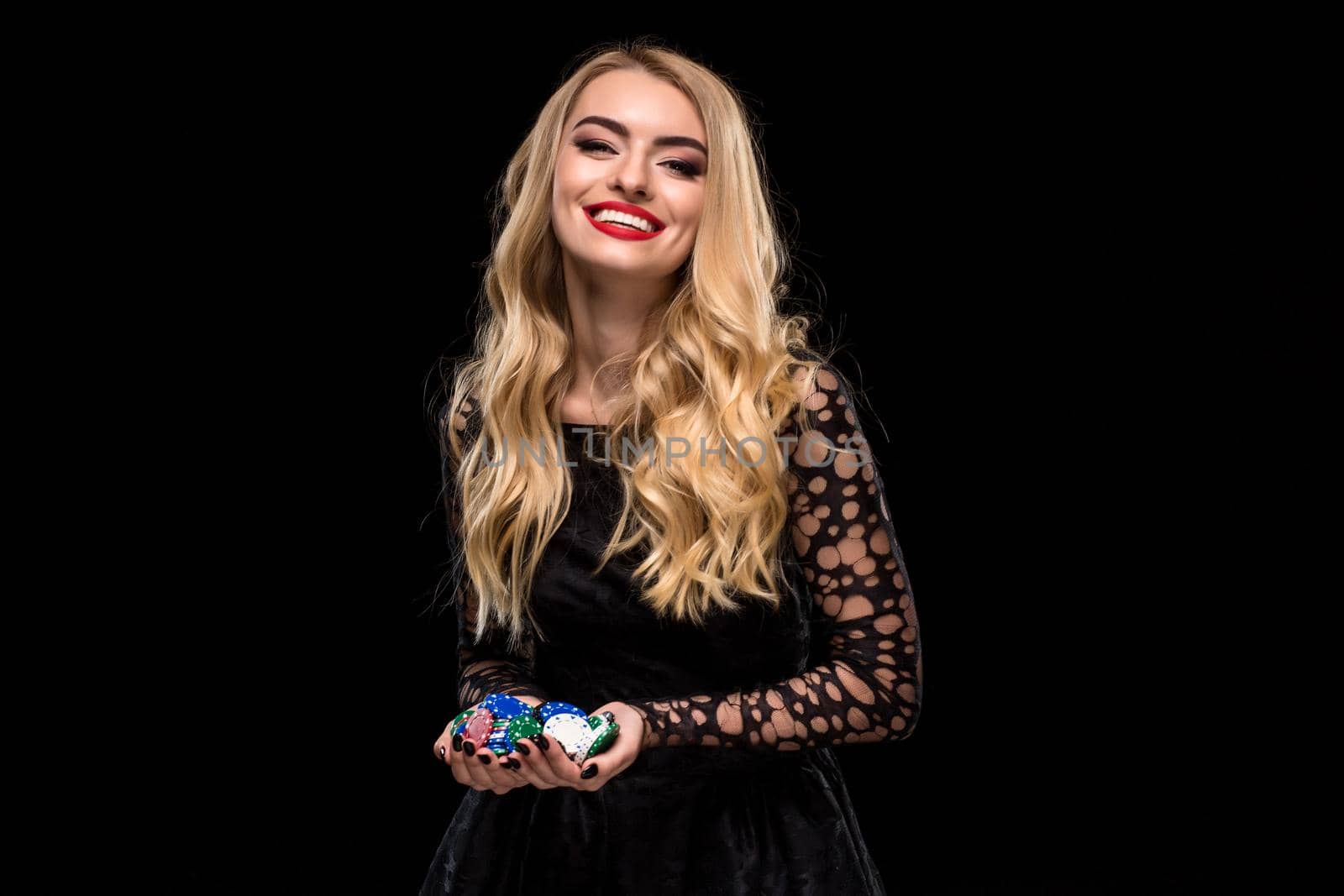 Elegant blonde in a black dress, casino player holding a handful of chips on black background. Poker. Casino. Roulette Blackjack Spin. Caucasian young woman looking at the camera emotions
