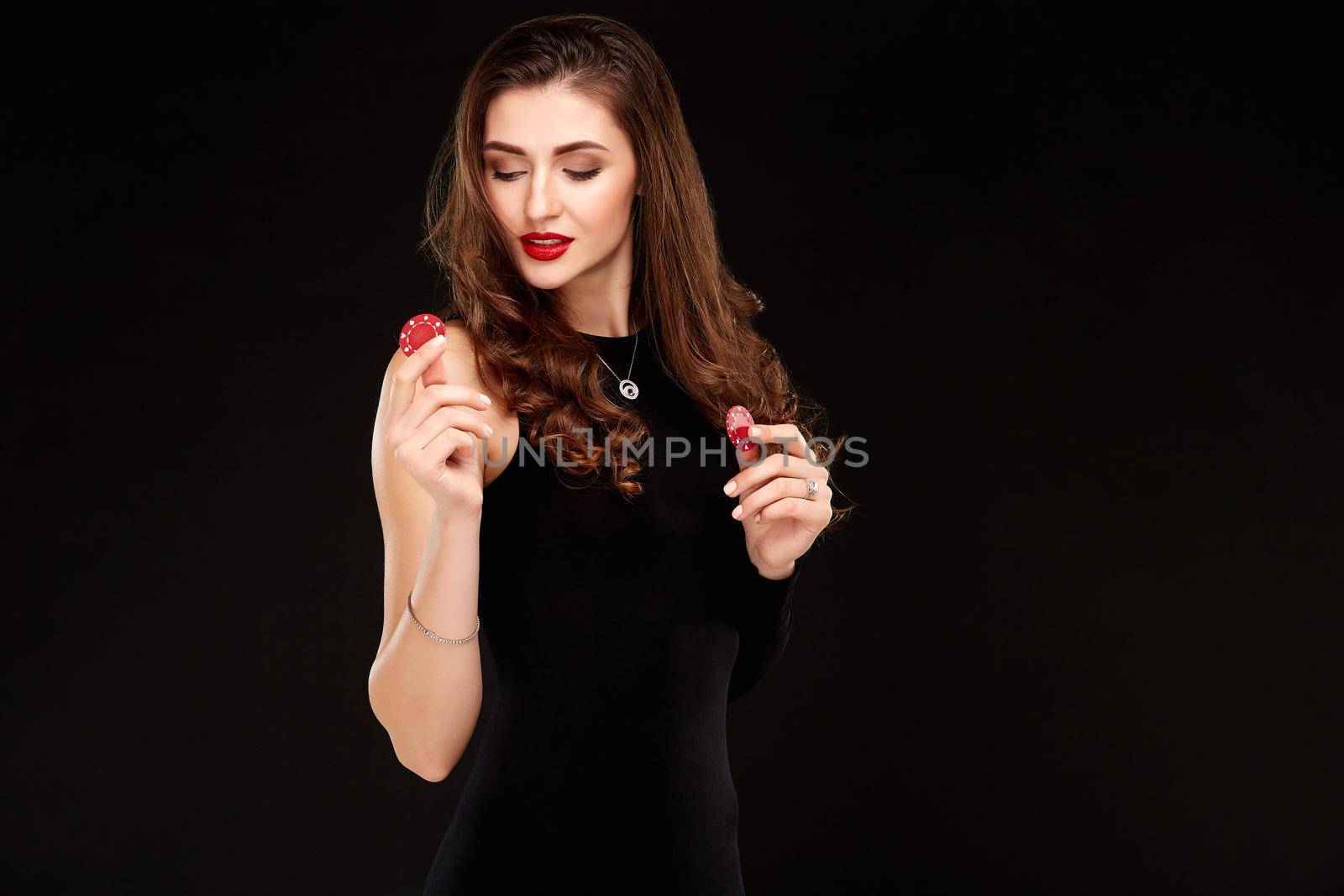 Sexy curly hair brunette in black dress posing with chips in her hands, poker concept black background. Casino, poker, Roulette Blackjack Spin.