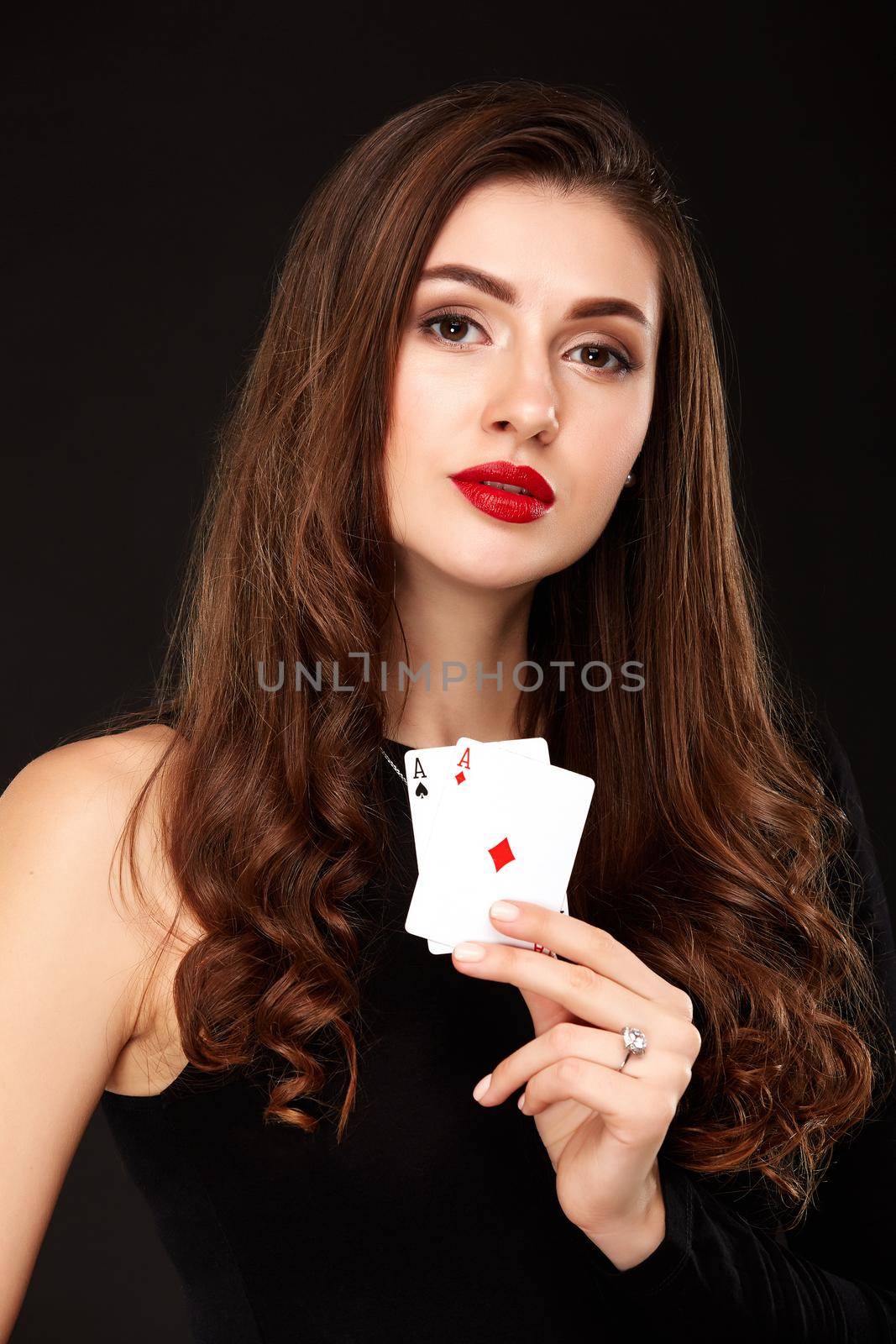 Sexy curly hair brunette in black dress posing with two aces cards in her hands, poker concept on black background. winning combination