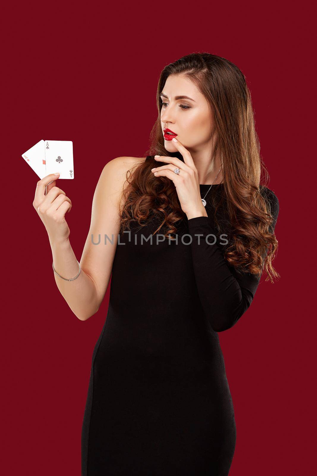 Beautiful caucasian woman in black dress with poker cards gambling in casino. Studio shot on red background. Poker. Two Aces in Hand