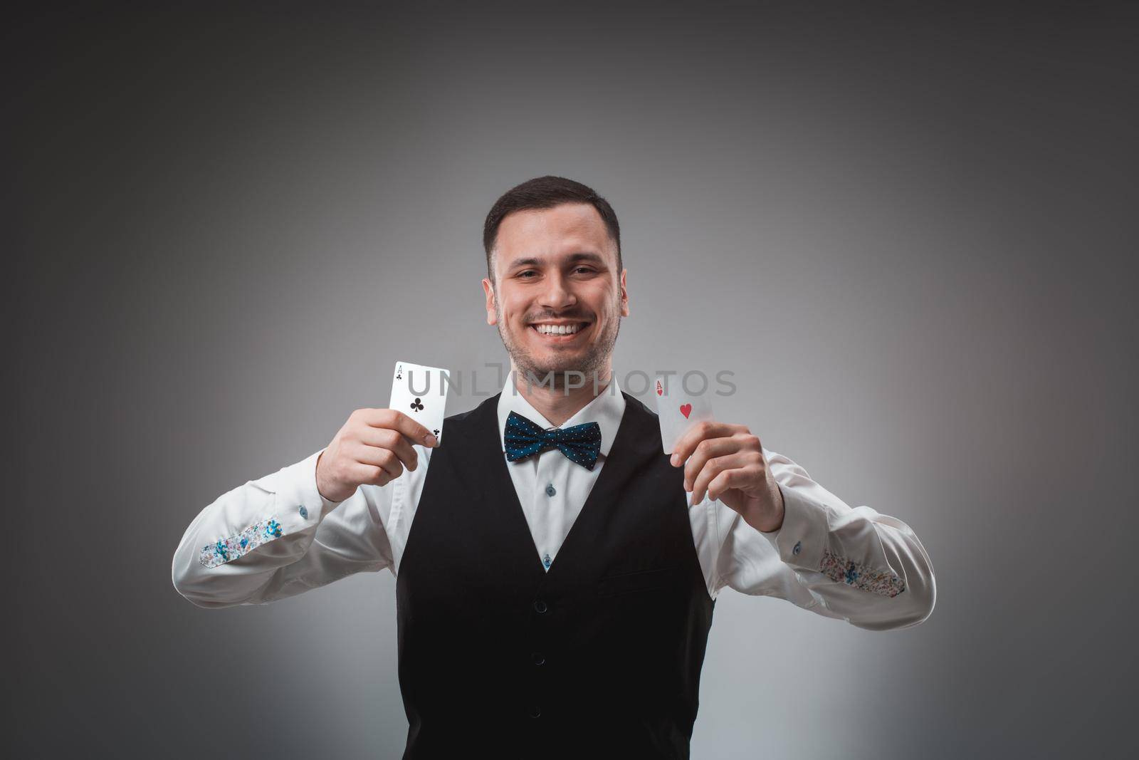 Handsome confident man holding cards looking at camera. Studio shot on gray background. Two Aces. Emotions happy