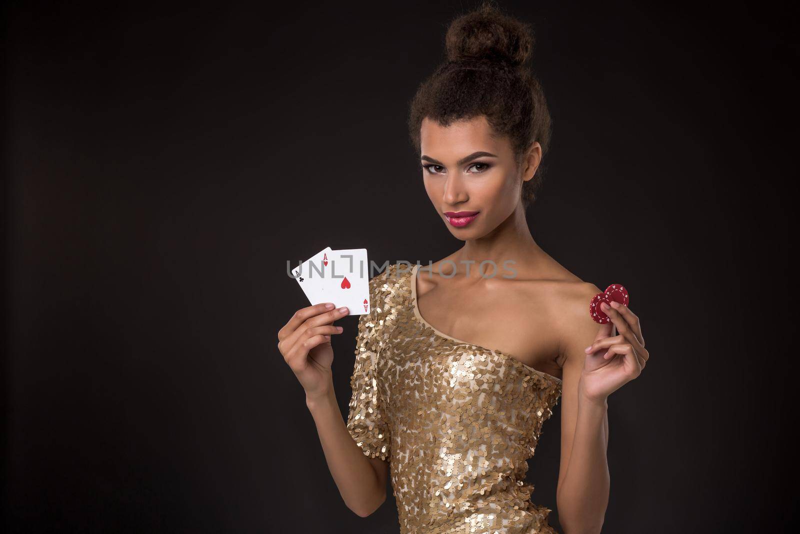 Woman winning - Young woman in a classy gold dress holding two aces and two red chips, a poker of aces card combination. Studio shot on black background