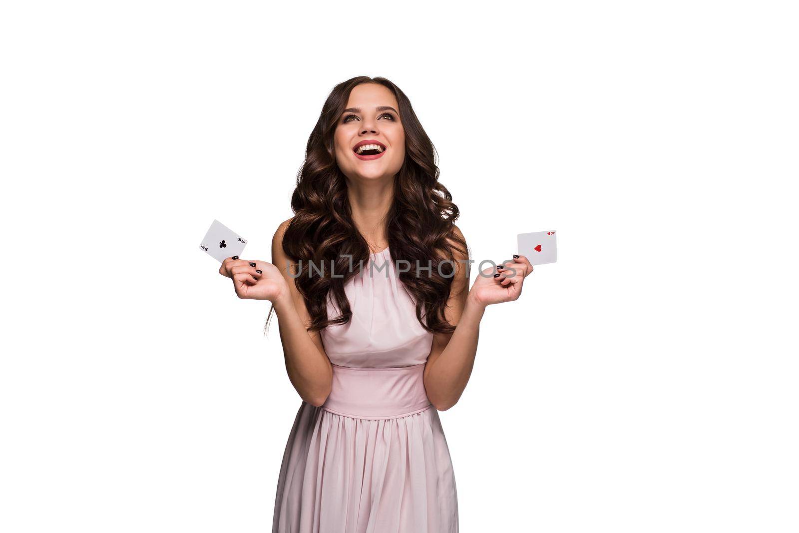 Beautiful confident woman in a sexy dress showing poker cards, looking up with copy place. Studio shot on white background. Casino