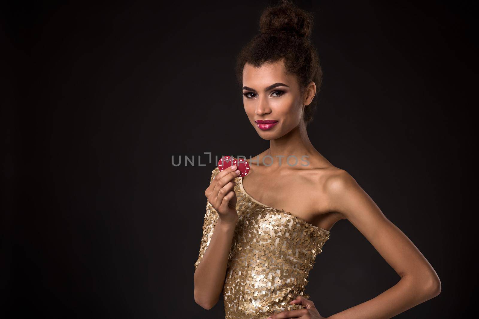 Woman winning - Young woman in a classy gold dress holding two red chips, a poker of aces card combination. Studio shot on black background