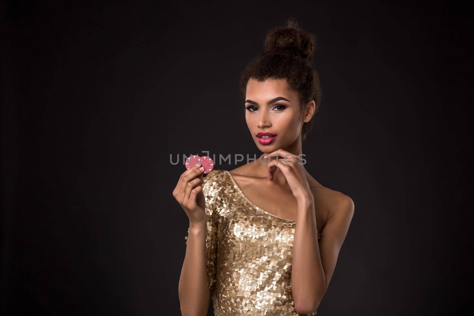 Woman winning - Young woman in a classy gold dress holding two red chips, a poker of aces card combination. Studio shot on black background