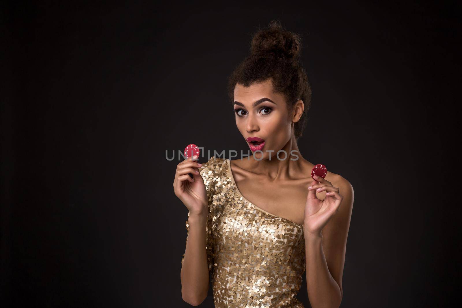 Woman winning - Young woman in a classy gold dress holding two red chips, a poker of aces card combination. Studio shot on black background