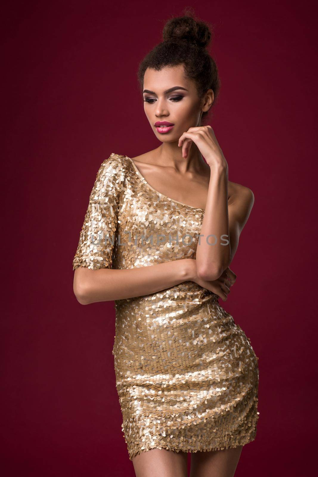 Fashion young African woman with makeup, in short sexy gold dress. Model on a red background in the studio
