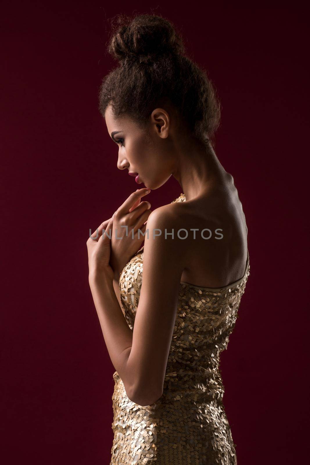 Fashion young African woman with make-up, in sexy gold dress. Model on a claret background in the studio. A woman is half a turn