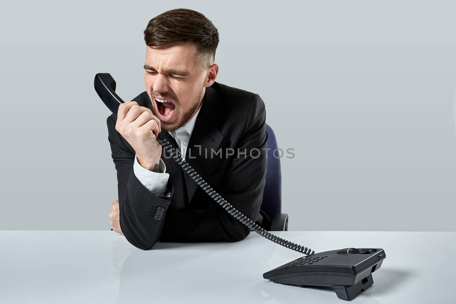 A young man in a black suit dials the phone number while sitting in the office. Manager talking on the phone. Man emotionally shouts