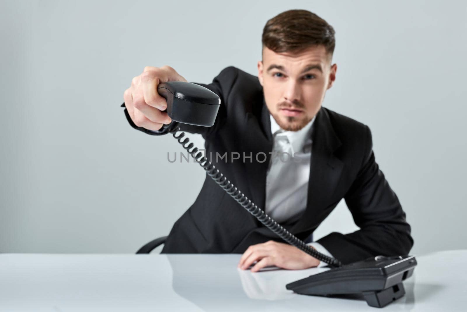 Portrait of attractive businessman holding telephone in his hand. This call is for you concept. A young man in a black suit dials the phone number while sitting in the office