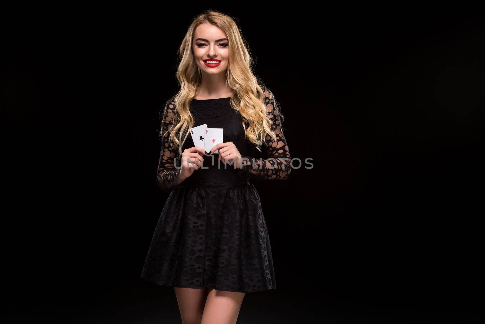 Beautiful young woman in black dress holding two ace of cards in her hand, isolated on black background. Poker. Casino. Roulette Blackjack Spin. Caucasian woman looking at camera