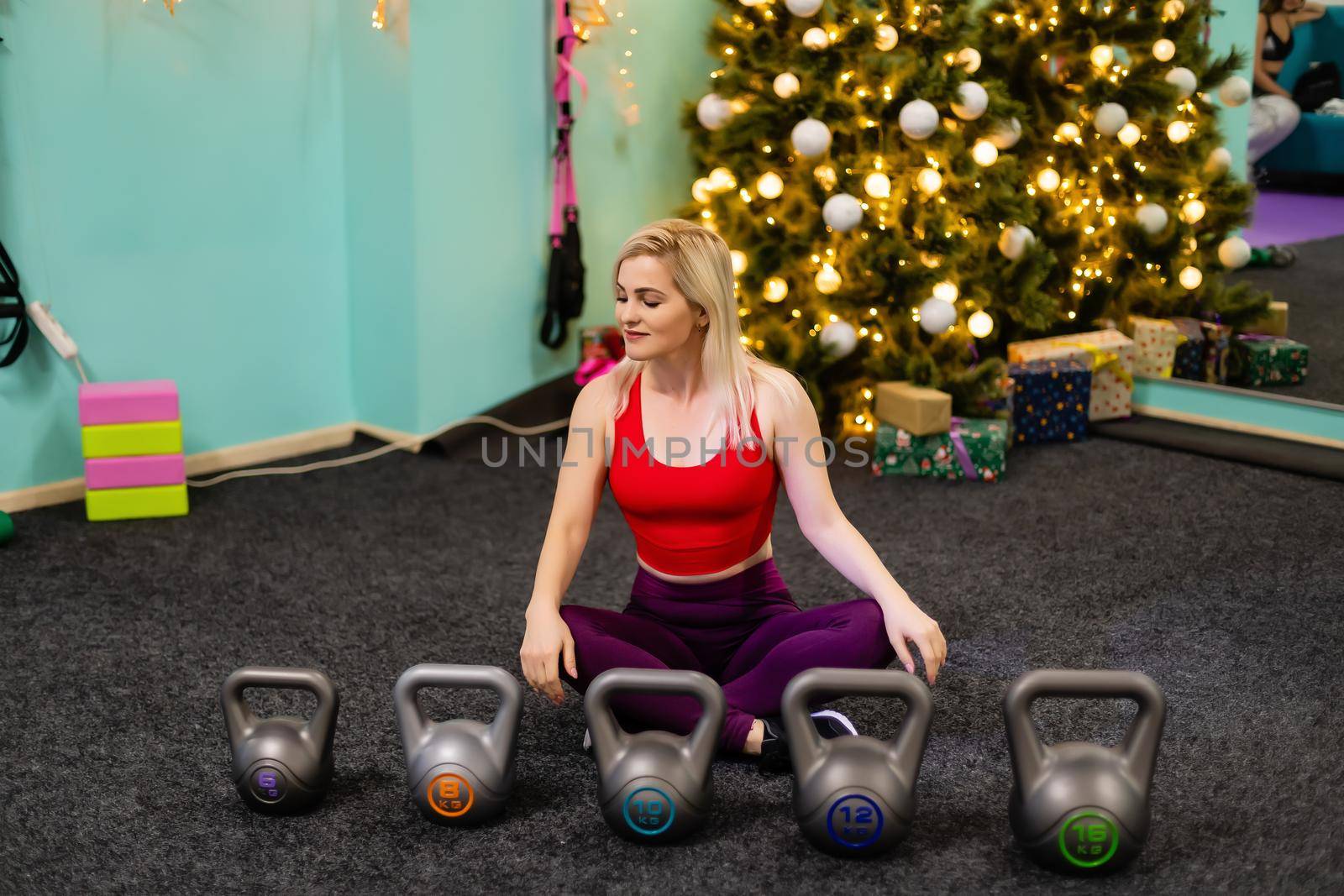 Christmas fitness woman smiling joyful and happy. Beautiful cheerful Caucasian female fitness model near christmas tree at the gym