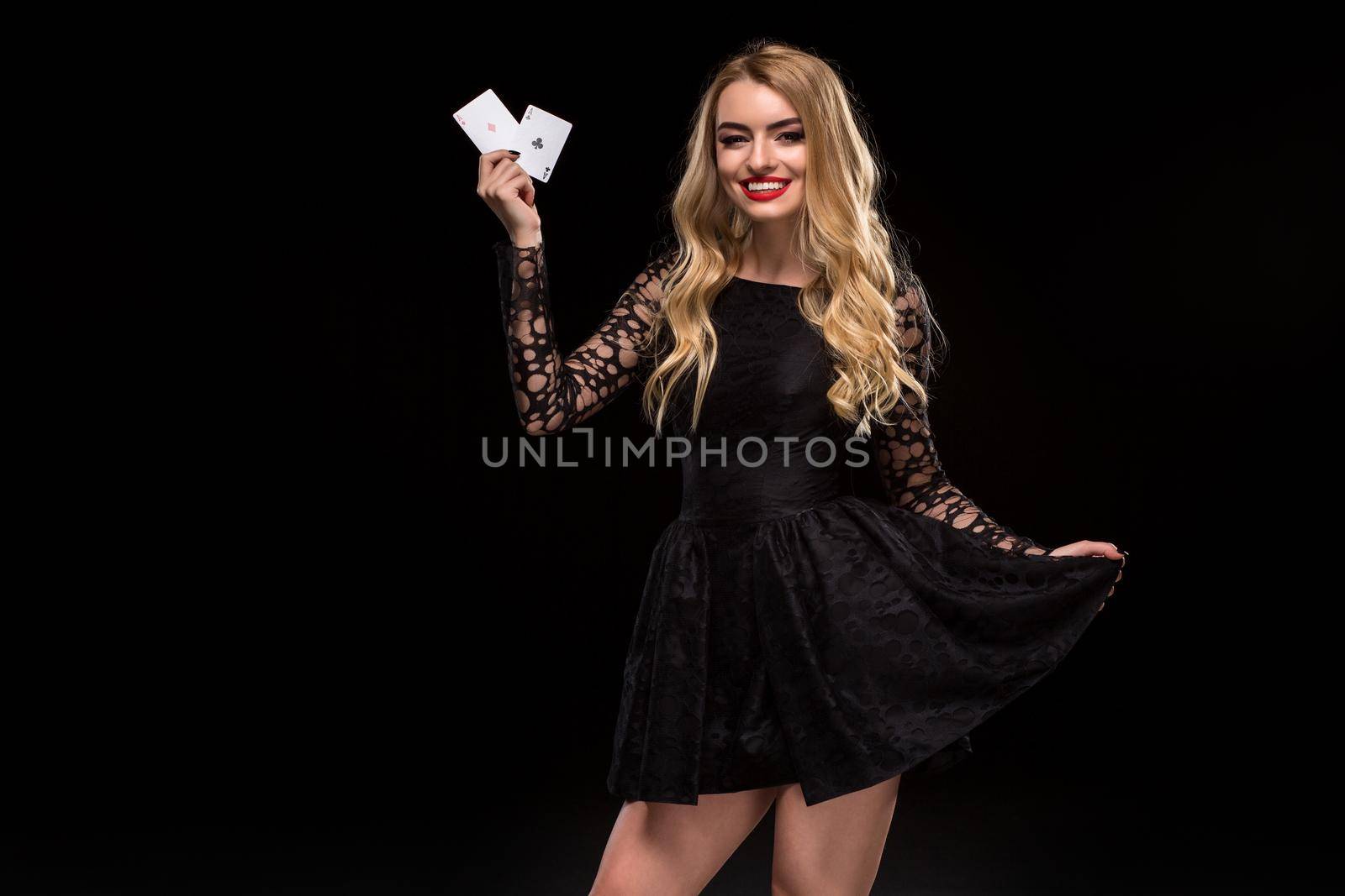 Beautiful young woman in black dress holding two ace of cards in her hand, isolated on black background. Poker. Casino. Roulette Blackjack Spin. Caucasian woman looking at camera