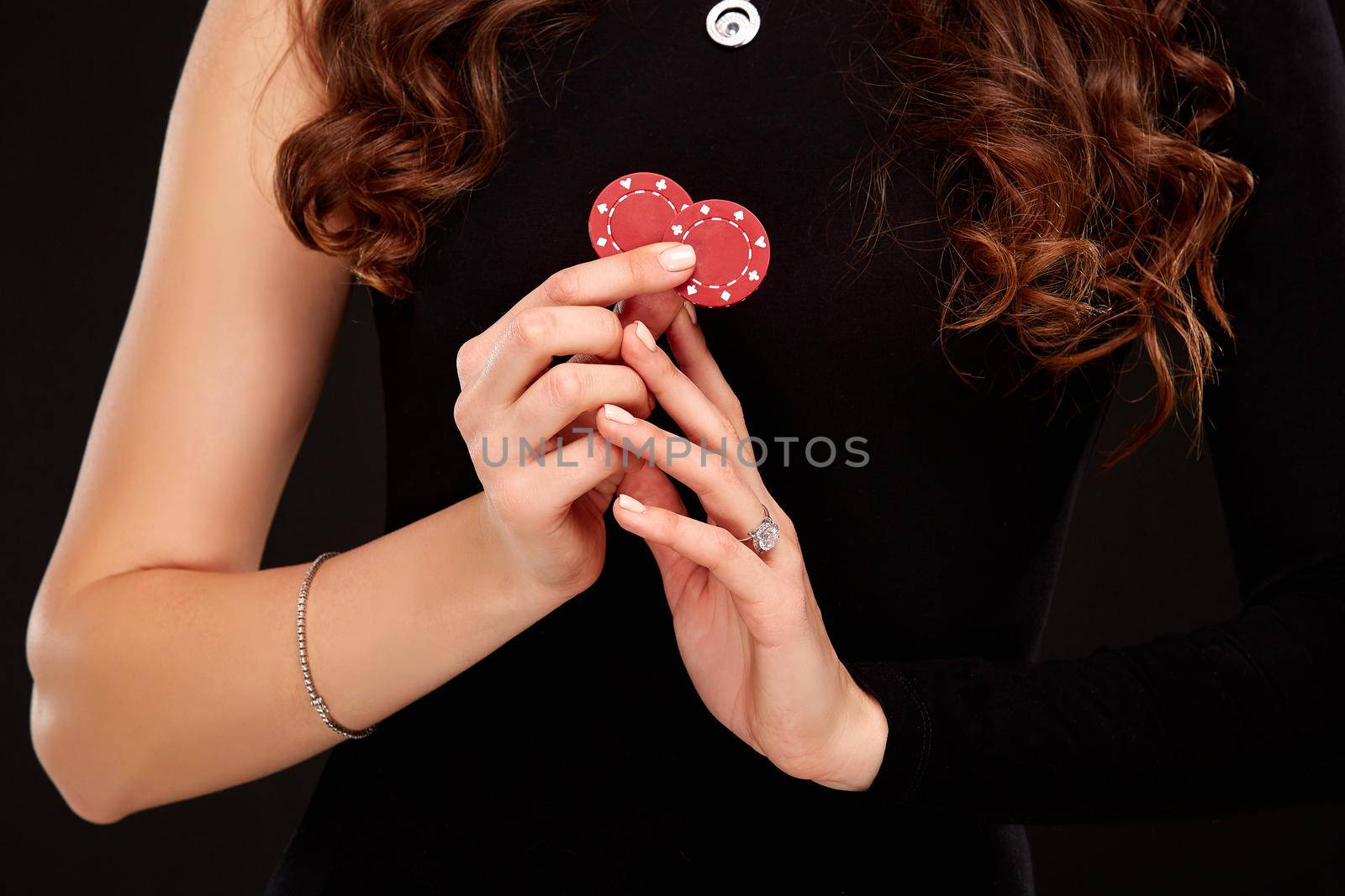 Sexy curly hair brunette in black dress posing with chips in her hands, poker concept black background. Casino, poker, Roulette Blackjack Spin.