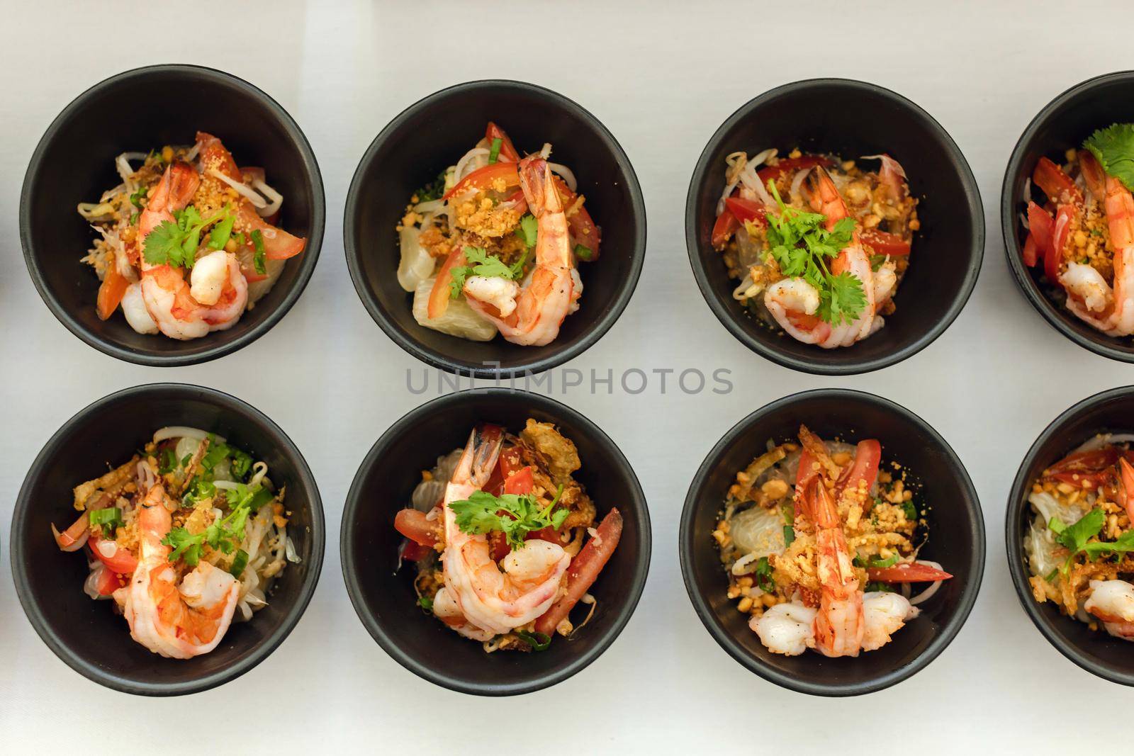 Top view of rows of seafood snack with shrimp in small black bowls on white background
