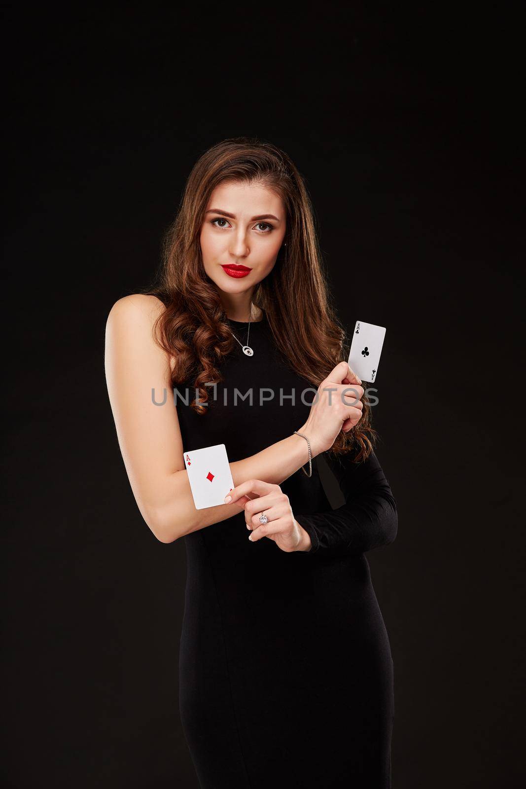 Attractive young woman in a sexy black dress holding the winning combination of poker cards. Two Aces. Studio shot on a black background. Casino