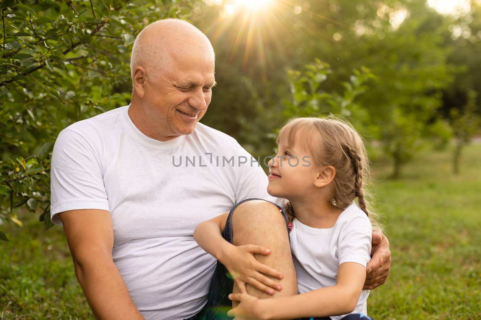 Portrait Of Grandfather With Granddaughter Relaxing Together in the garden by Andelov13