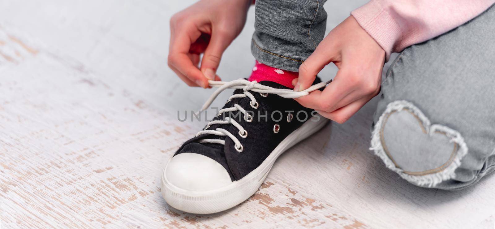 Little girl sitting on the floor and tying shoelaces on her black and white colour snikers