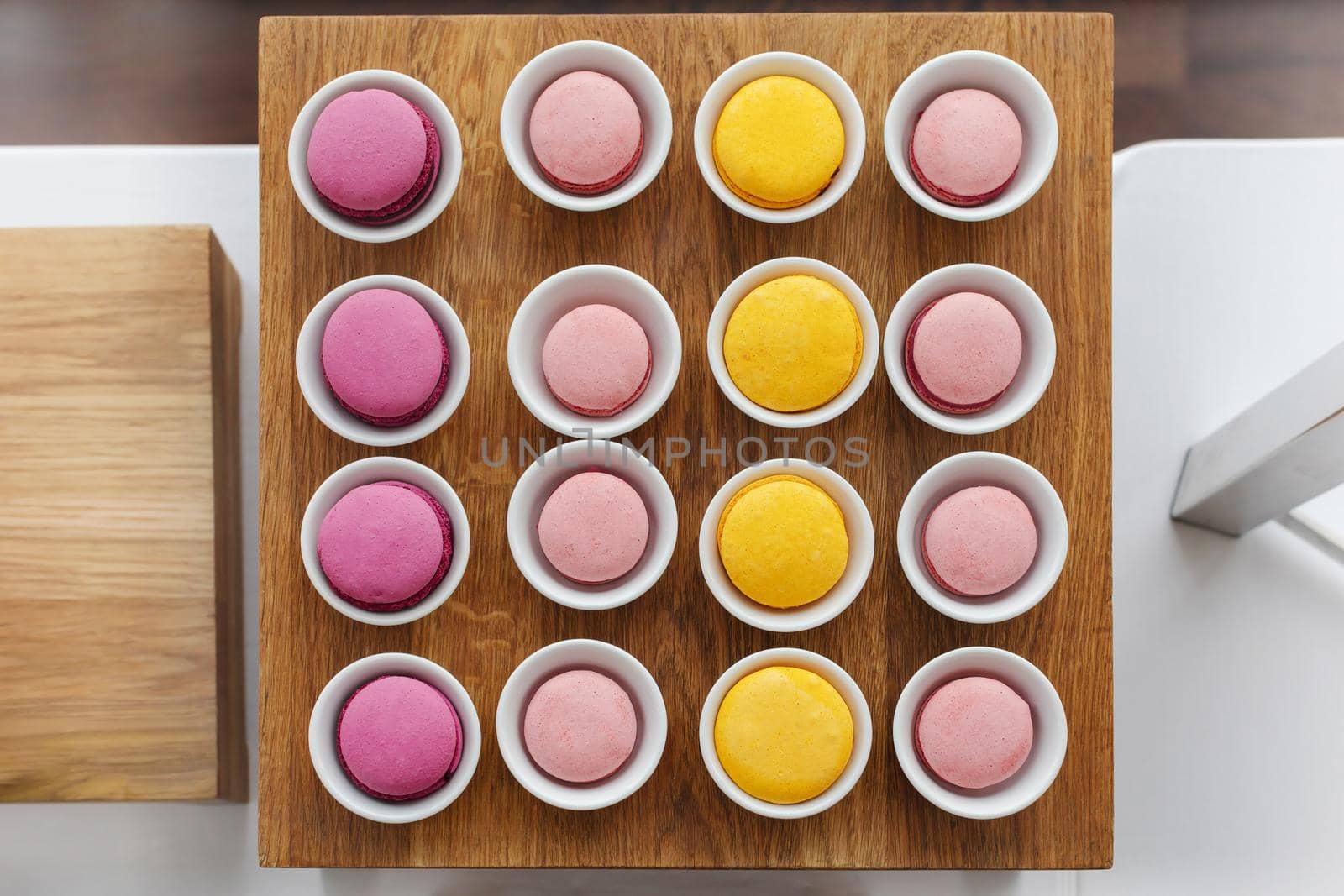 Top view of colourful macaroons served in cups arranged in even square shape on wooden stand