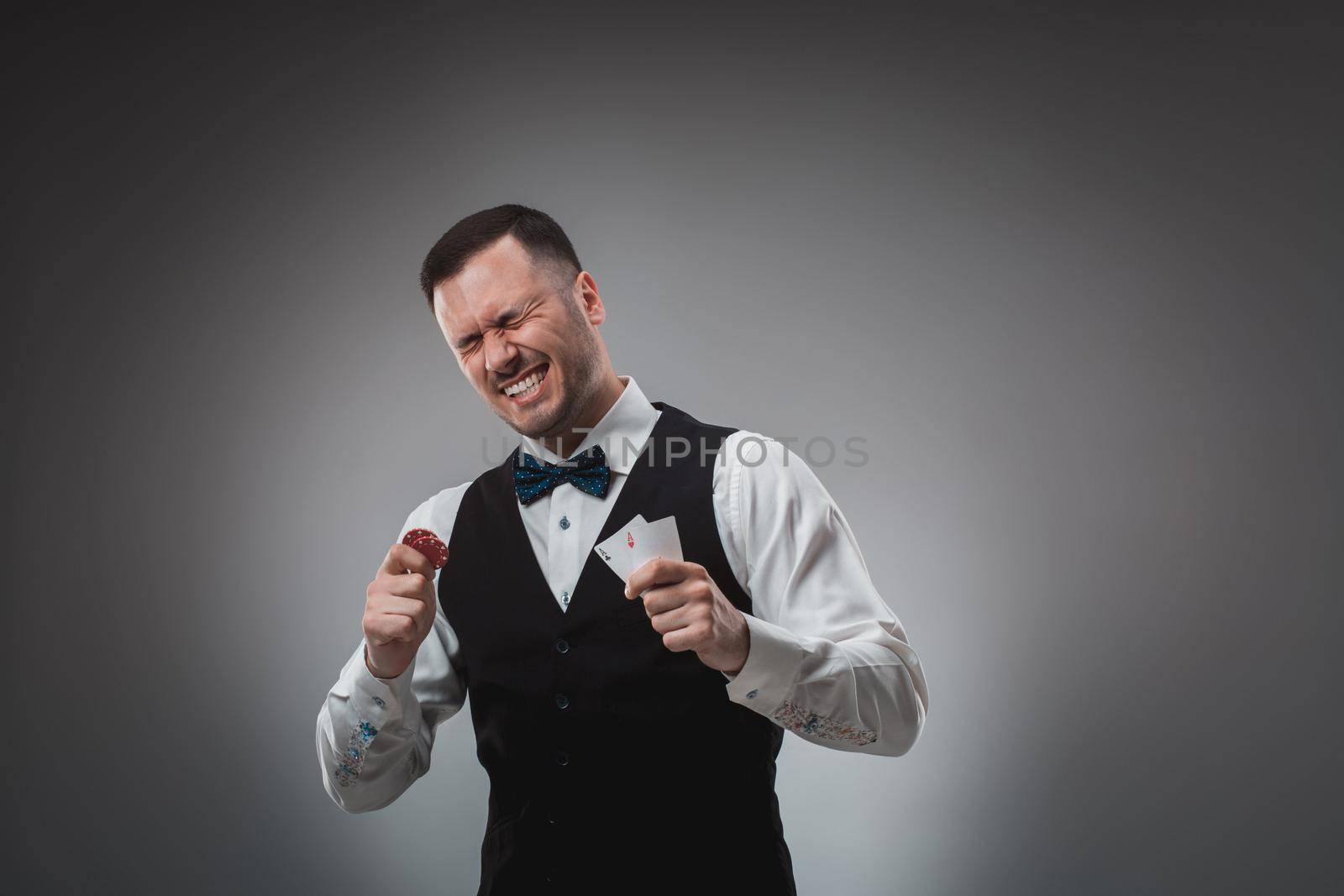 Young man in shirt and waistcoat shows his cards and holds poker chips in his hands, studio shot. Poker. Emotions