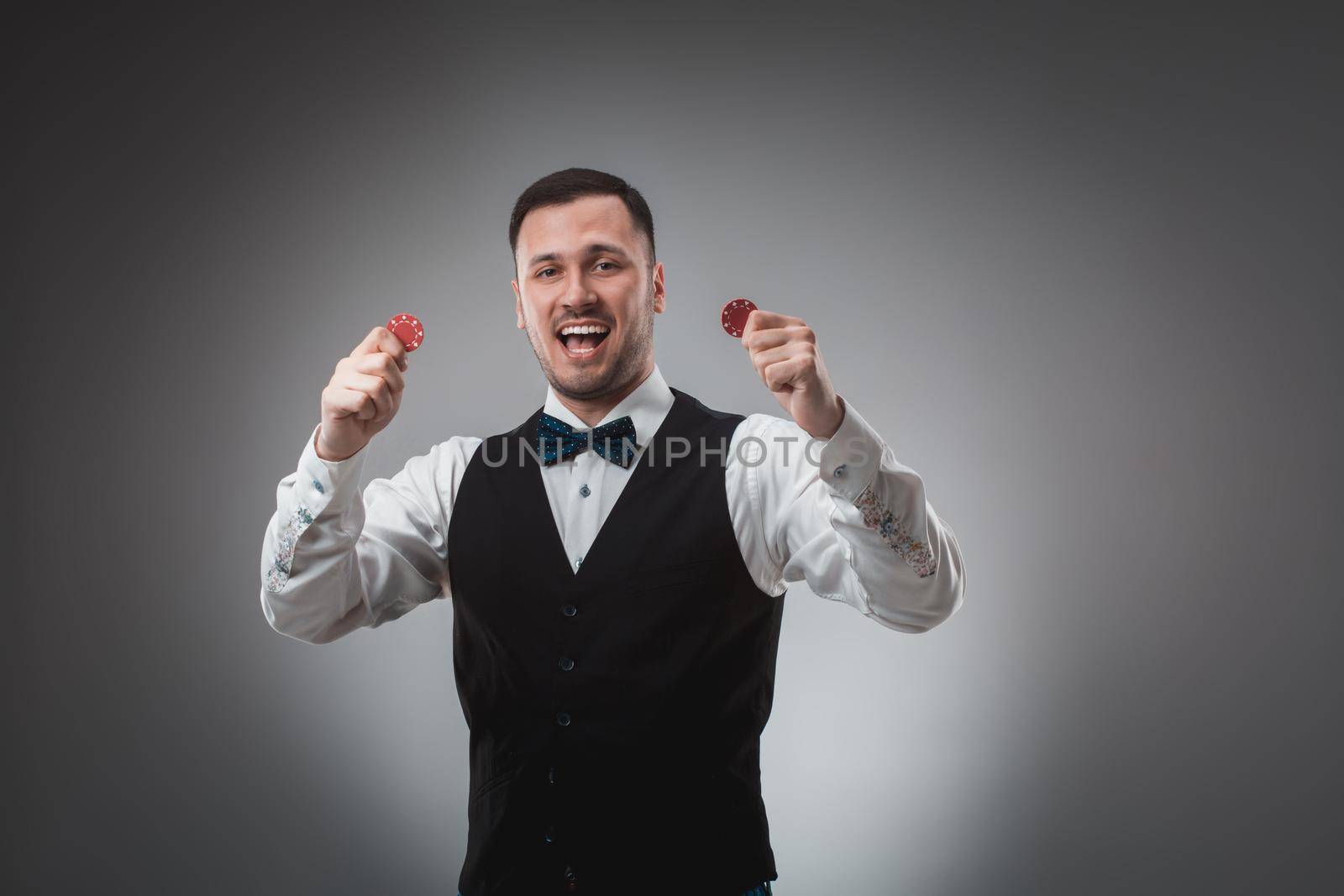 A man holding up red poker chips. Man in shirt and butterfly in studio on gray background. Poker