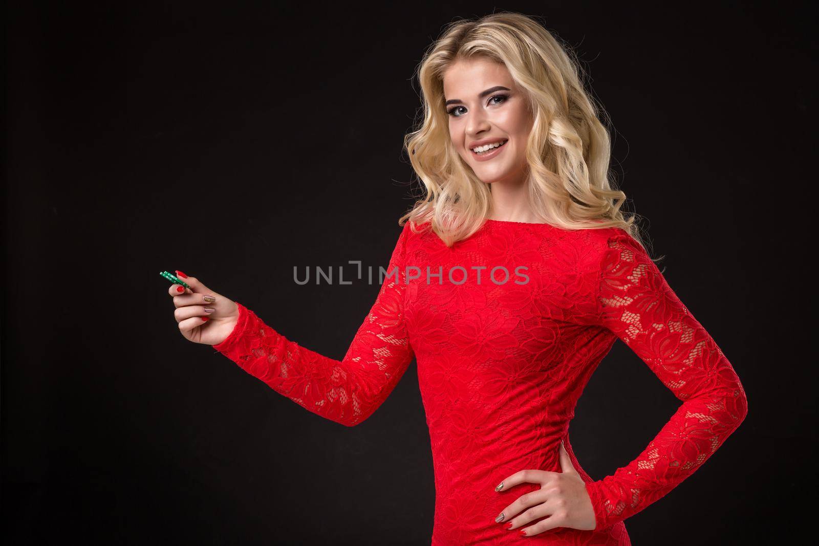 Young beautiful blond woman in a red dress with poker chips over black. Poker