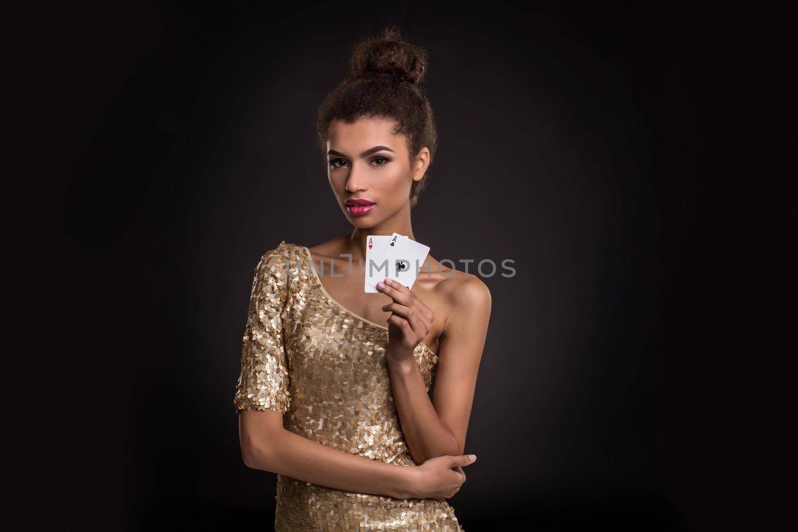 Woman winning - Young woman in a classy gold dress holding two aces, a poker of aces card combination. Studio shot on black background