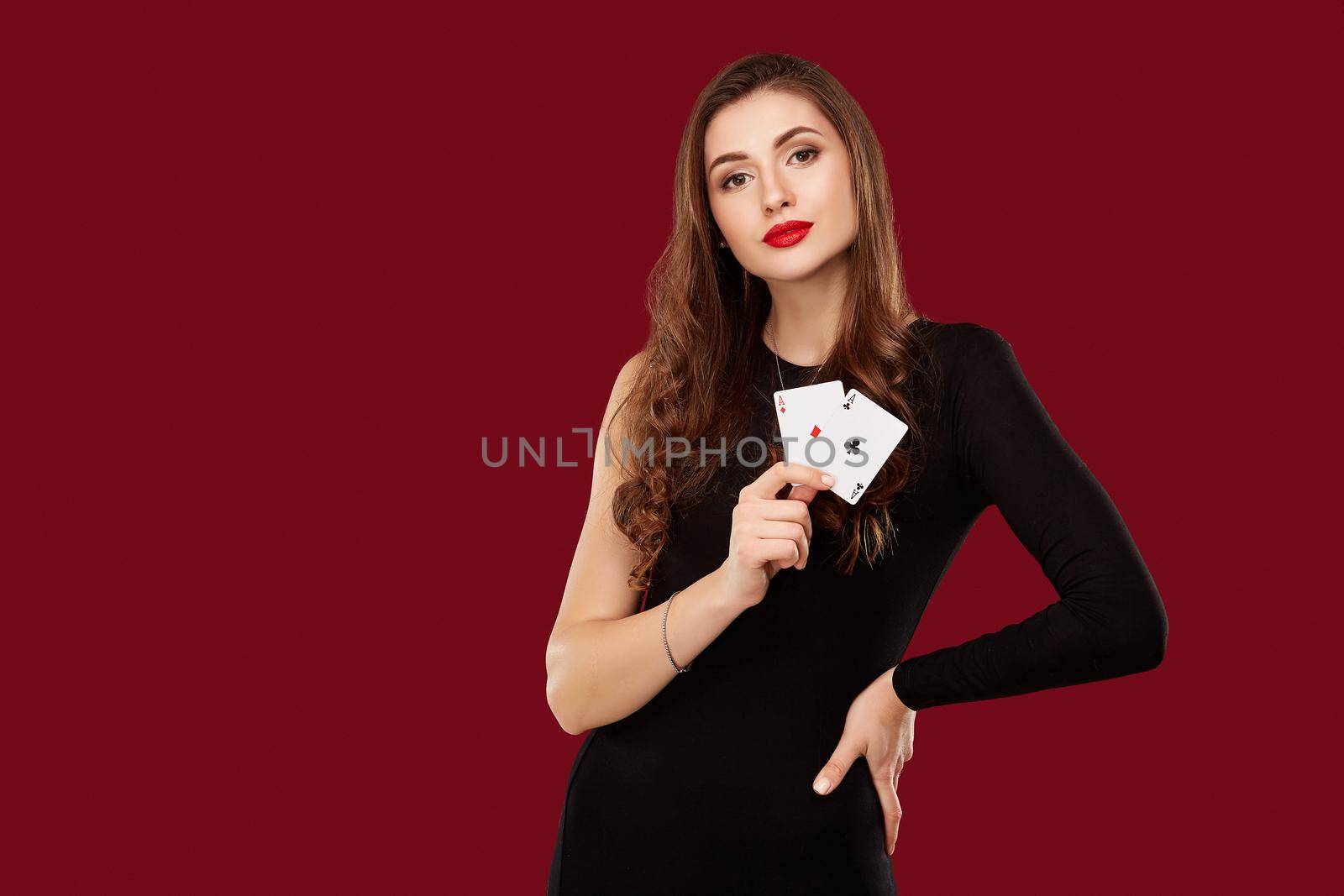 Beautiful caucasian woman in black dress with poker cards gambling in casino. Studio shot on red background. Poker. Two Aces in Hand