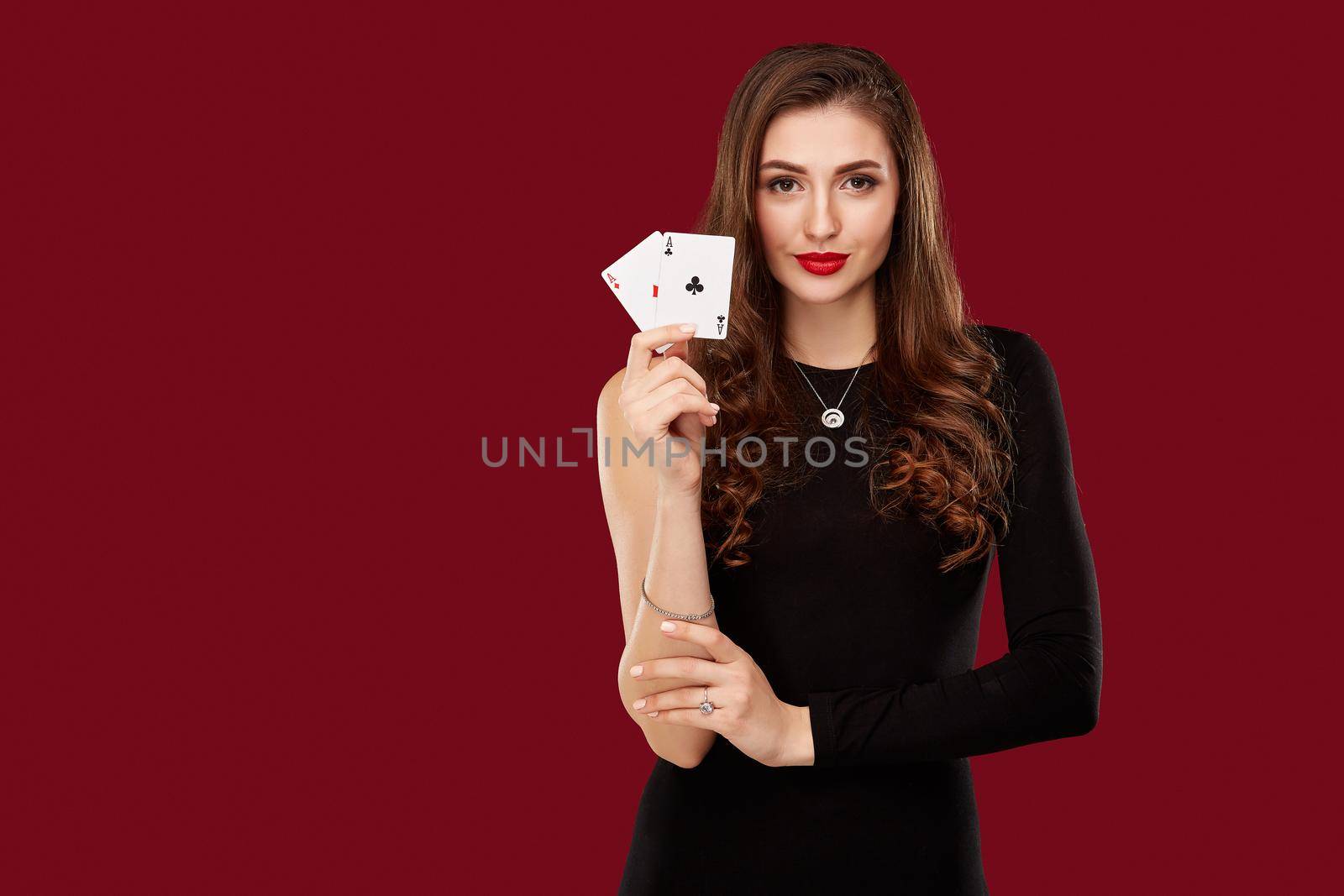Beautiful caucasian woman in black dress with poker cards gambling in casino. Studio shot on red background. Poker. Two Aces in Hand