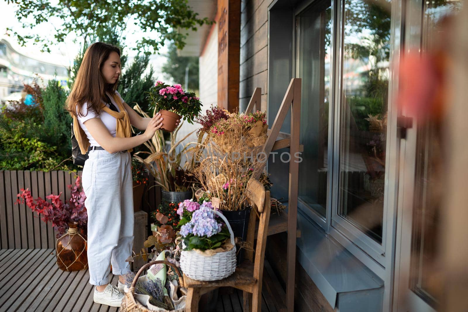 happy caucasian young woman chooses potted flowers to buy at outdoor garden stall.