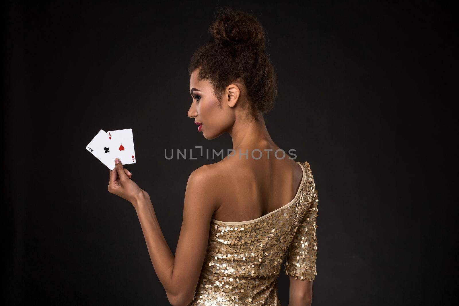 Woman winning - Young woman in a classy gold dress holding two aces, a poker of aces card combination. Studio shot on black background. A young woman stands with her back