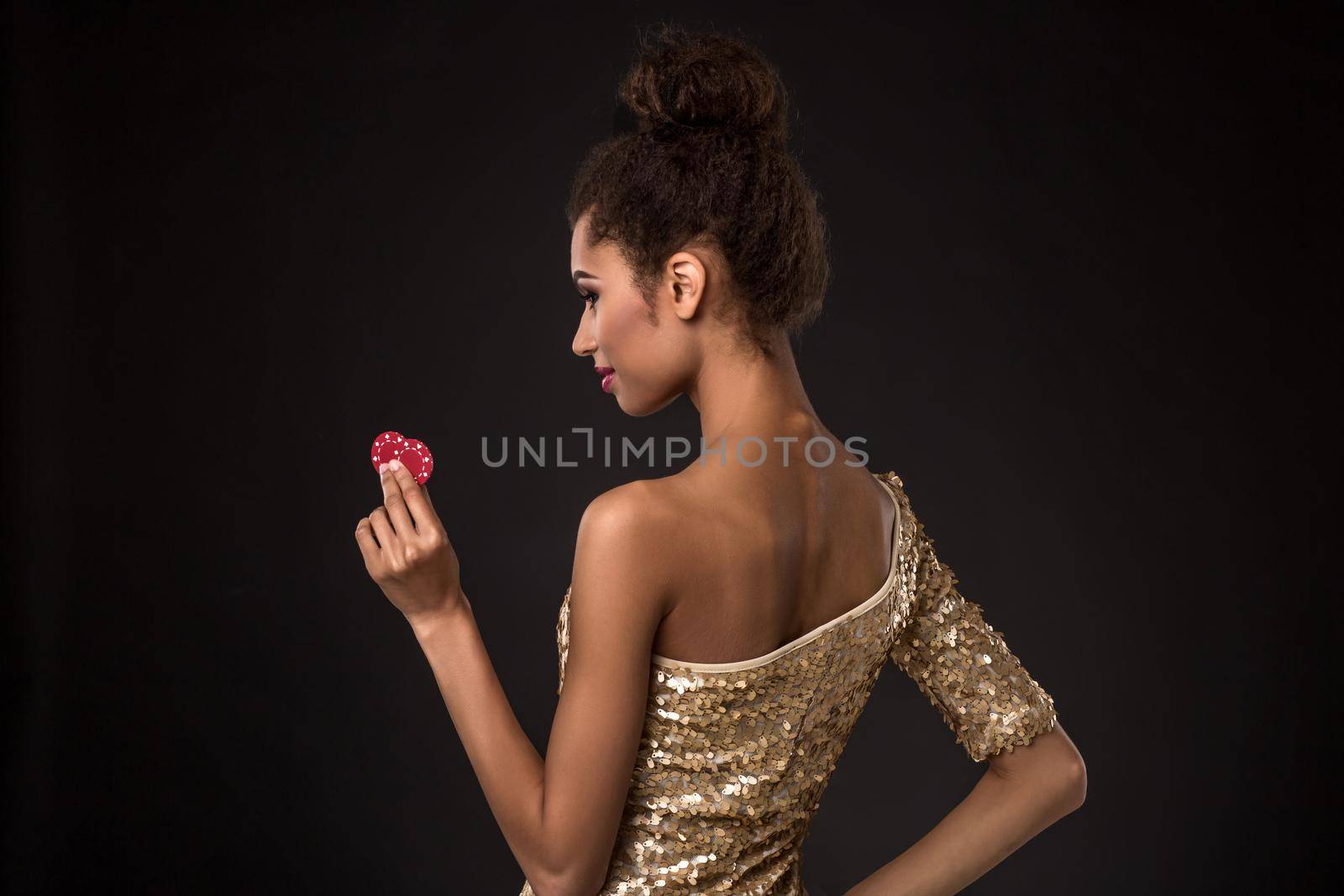 Woman winning - Young woman in a classy gold dress holding two red chips, a poker of aces card combination. Studio shot on black background. A young woman stands with her back