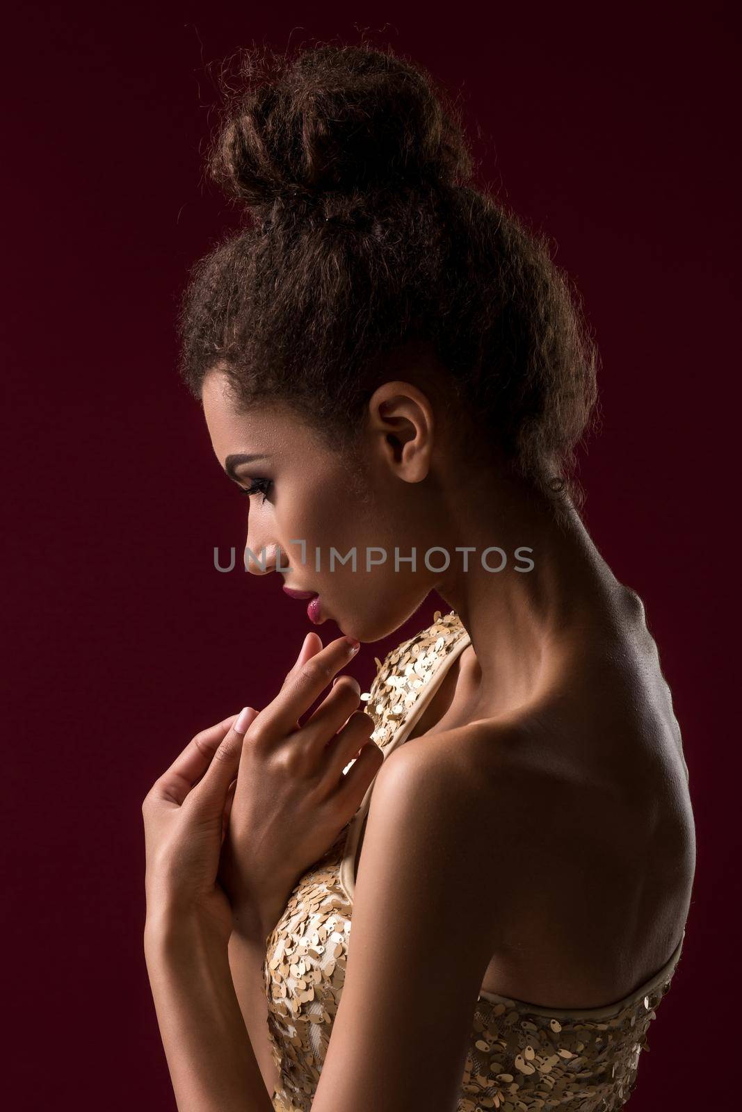 Fashion young African woman with make-up, in sexy gold dress. Model on a claret background in the studio. A woman is half a turn