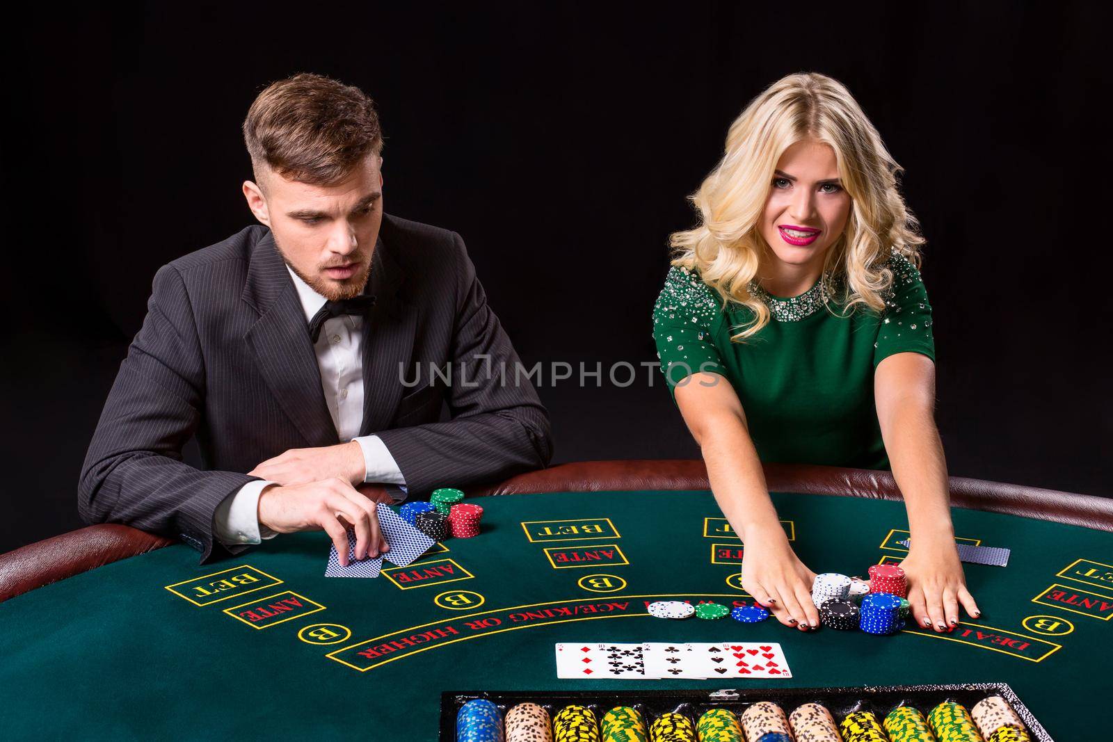 couple playing poker at the green table. The blonde girl and a guy in a suit. all-in bets chips