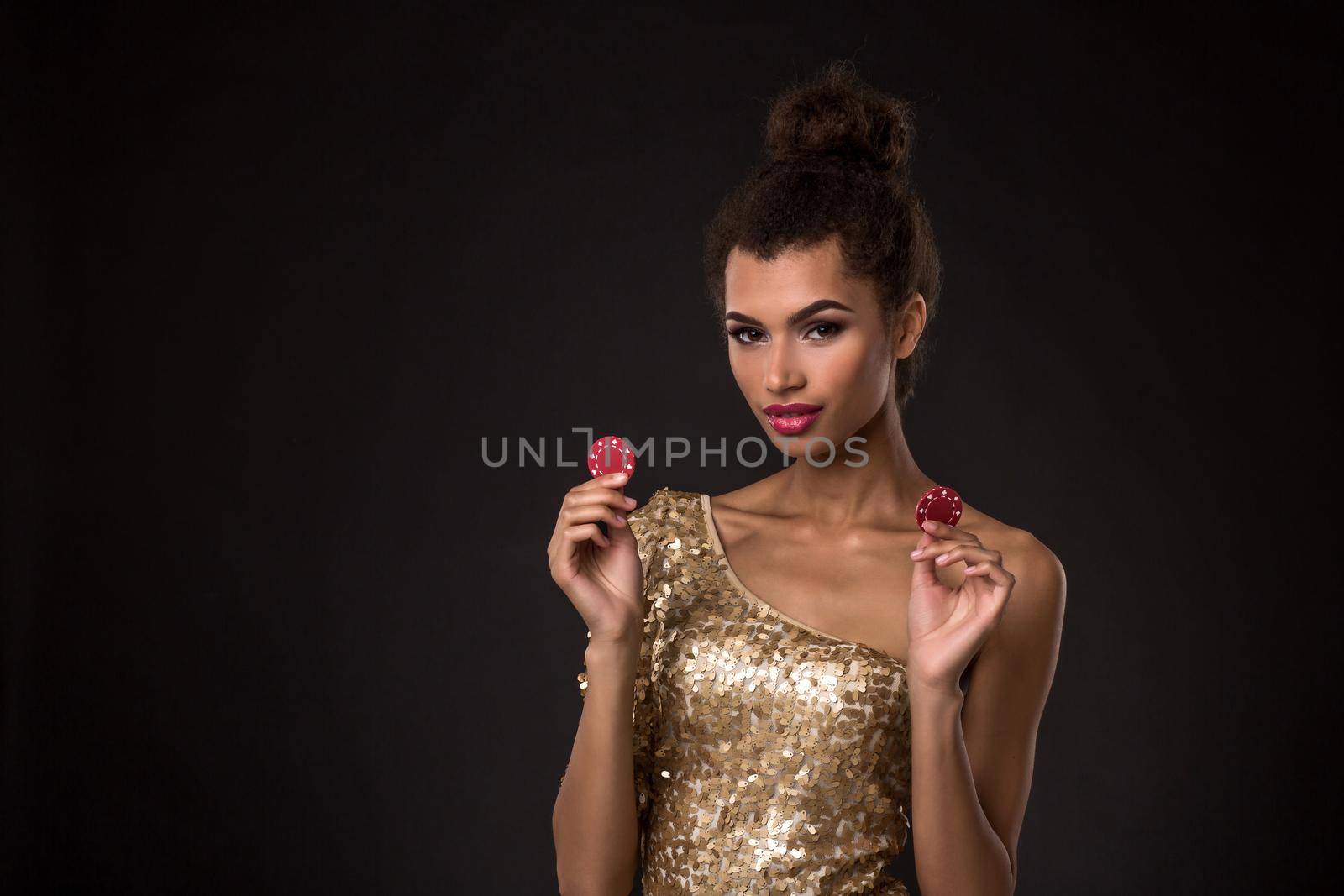 Woman winning - Young woman in a classy gold dress holding two red chips, a poker of aces card combination. Studio shot on black background