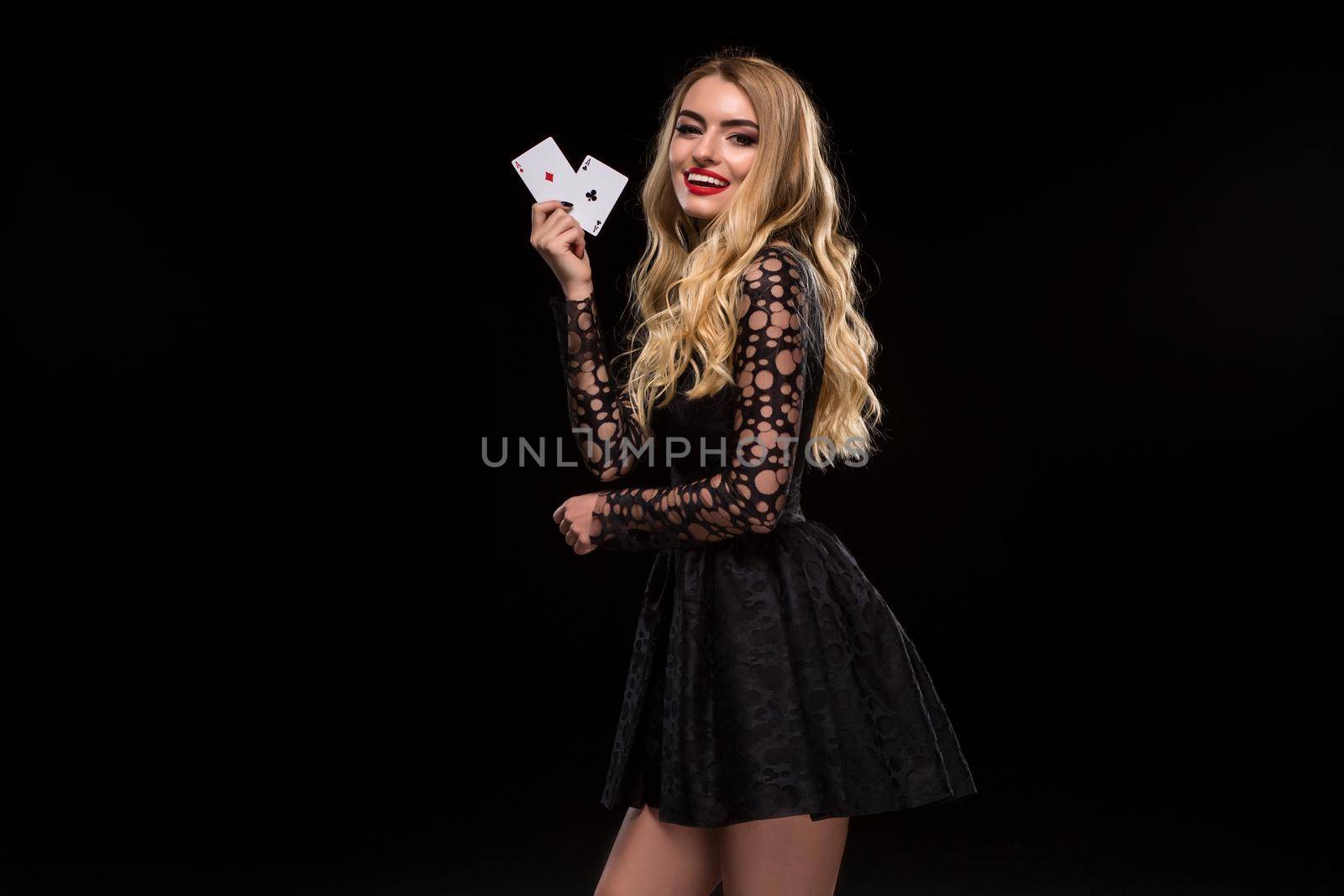 Beautiful young woman in black dress holding two ace of cards in her hand, isolated on black background. Poker. Casino. Roulette Blackjack Spin. Caucasian woman looking at camera